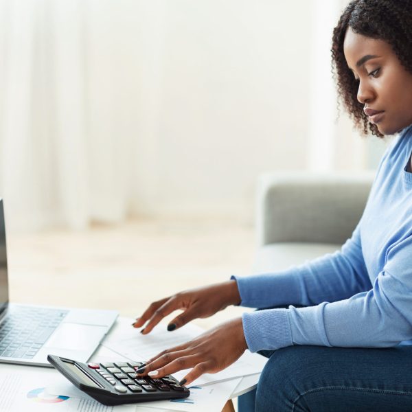 Business Concept. African American female accounting analyst calculating income and expenses for financial report and banking investment. Black woman using laptop computer at home office