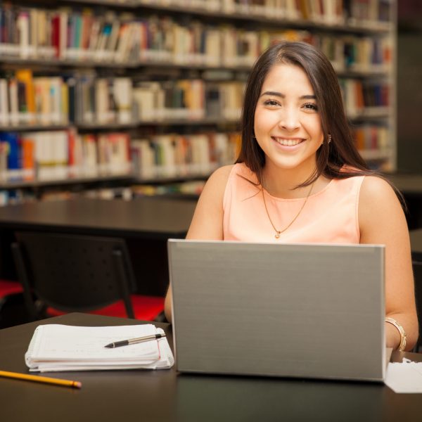 Portrait of a young brunette using a laptop computer for school work in the library and smiling